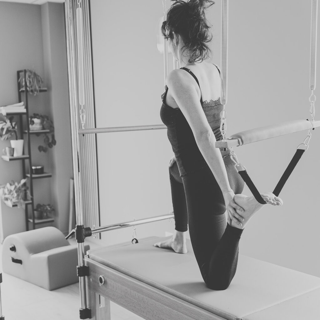 Kobieta wykonuje ćwiczenie rozciągające na reformerze Pilates w jasnym studiu